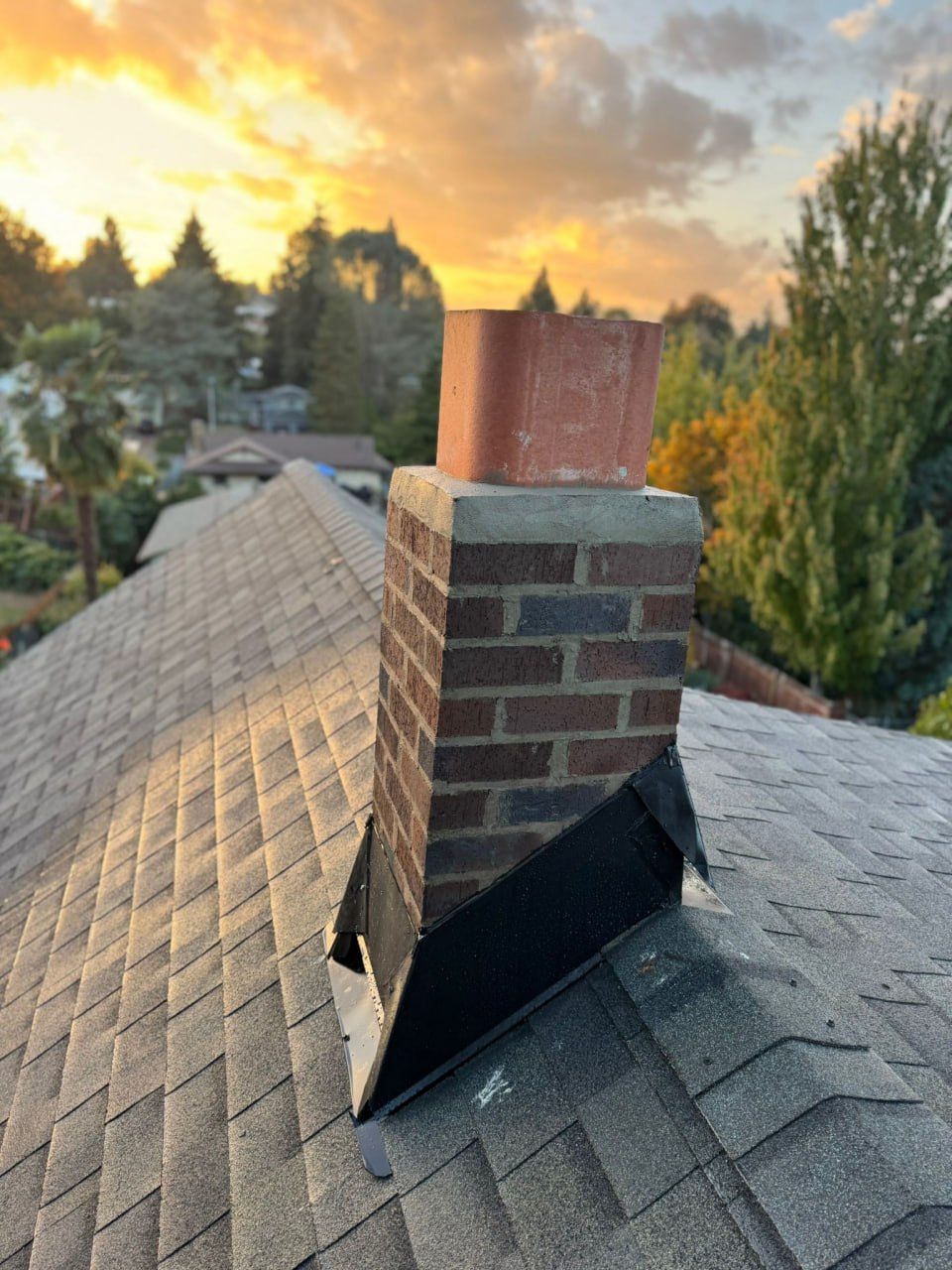 A brick chimney at sunset with a rebuilt crown, clay flue and new lead flashing