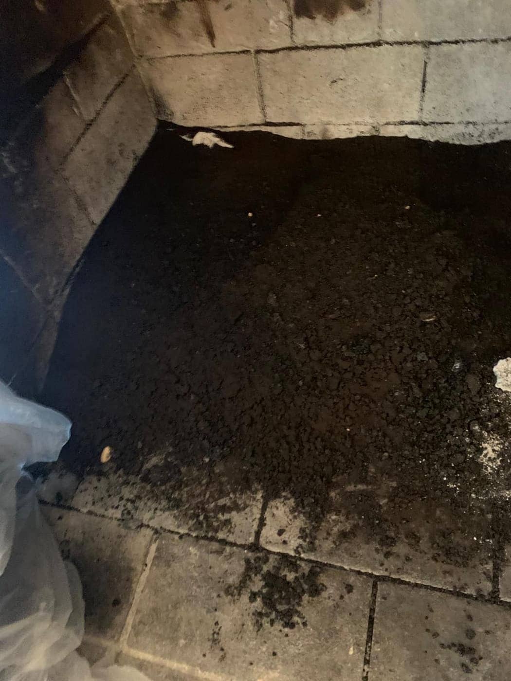 El piso de una cámara de combustión cubierto de hollín y escombros, entre paredes de ladrillo refractario claro.
