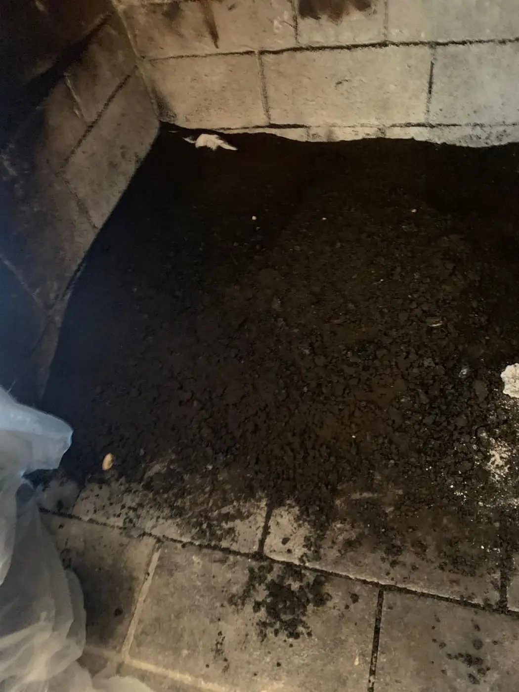 El piso de una cámara de combustión cubierto de hollín y escombros, entre paredes de ladrillo refractario claro.