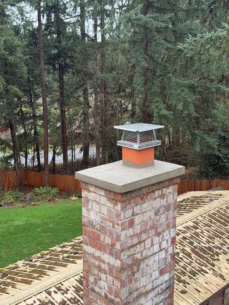 An exterior brick chimney with its cap in place, seen from the garden