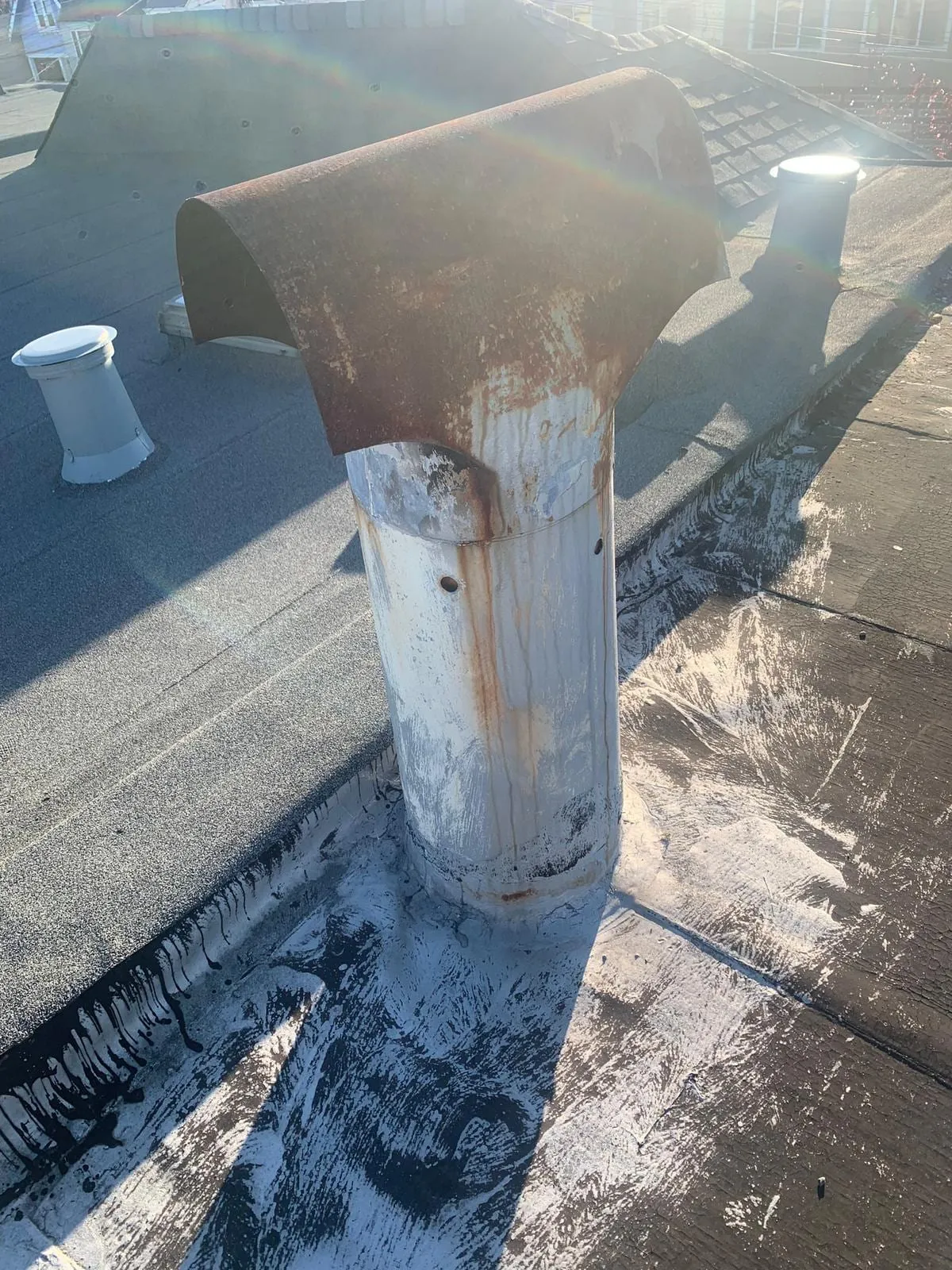 A rusted flue cap on a flat roof after a New Jersey winter