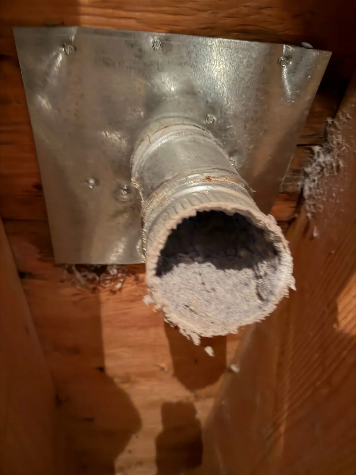 A dryer duct stub packed with lint, seen from below a basement ceiling